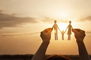 Hands holding paper cutout of parents and child under sunset for family law